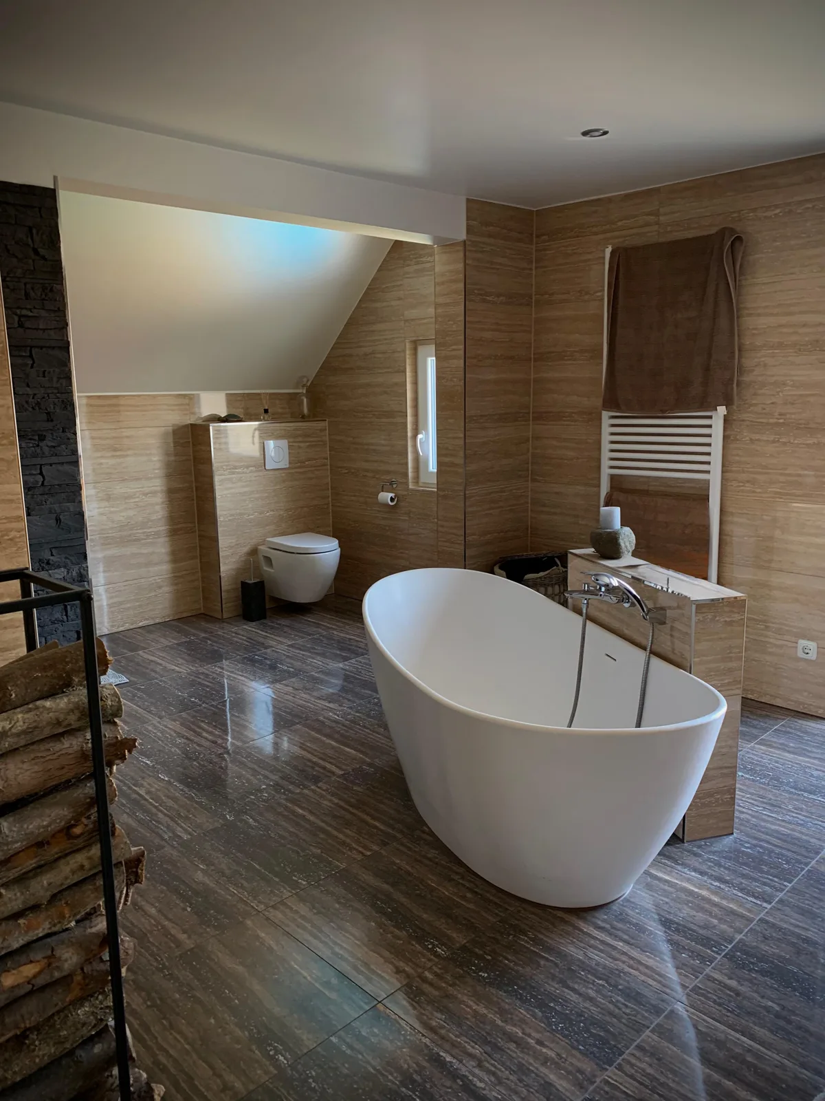Dachgeschossbad mit freistehender Badewanne und großformatigen Fliesen in Travertin-Optik