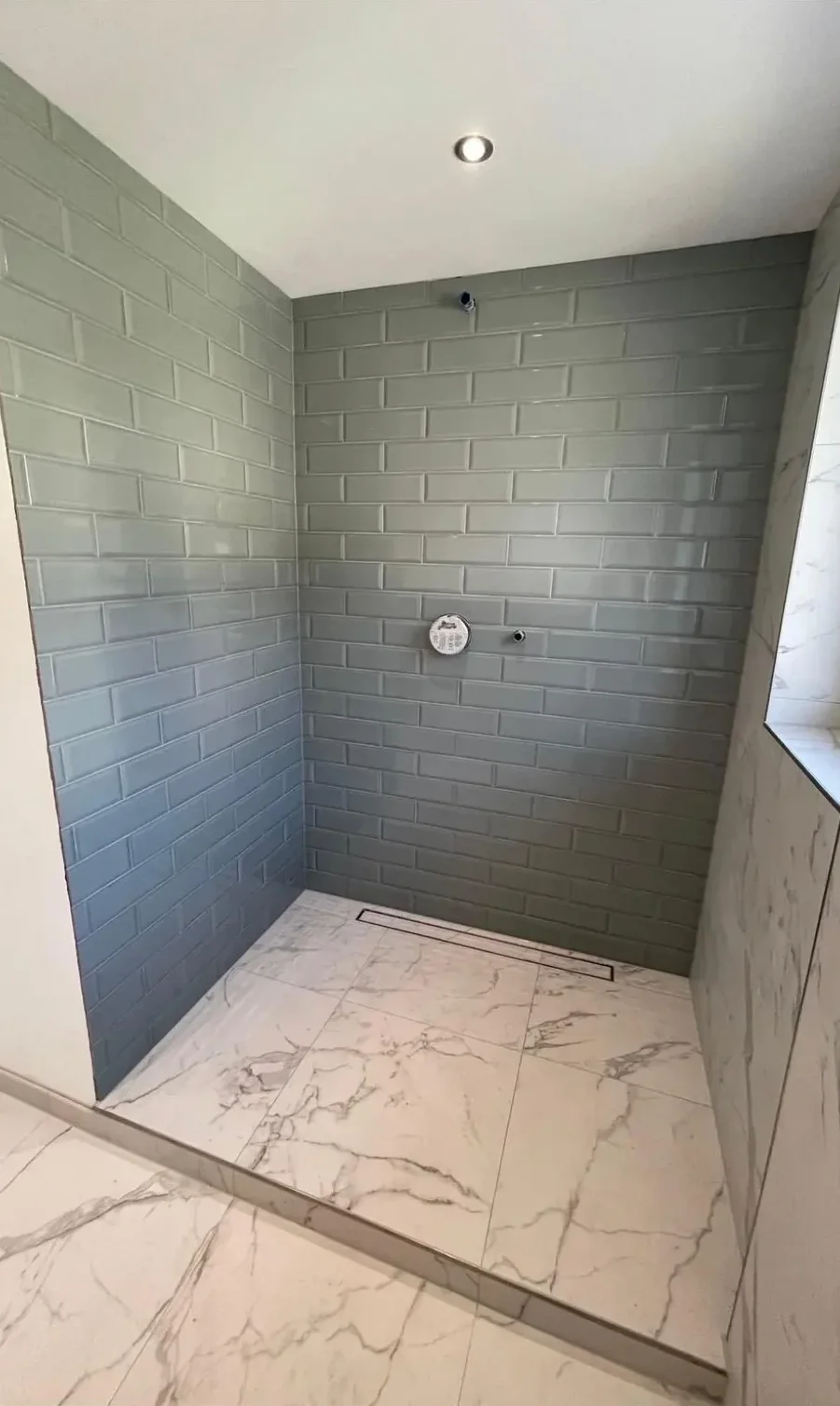 Dusche mit grünen Metrofliesen an der Wand und Bodenfliesen in Marmoroptik