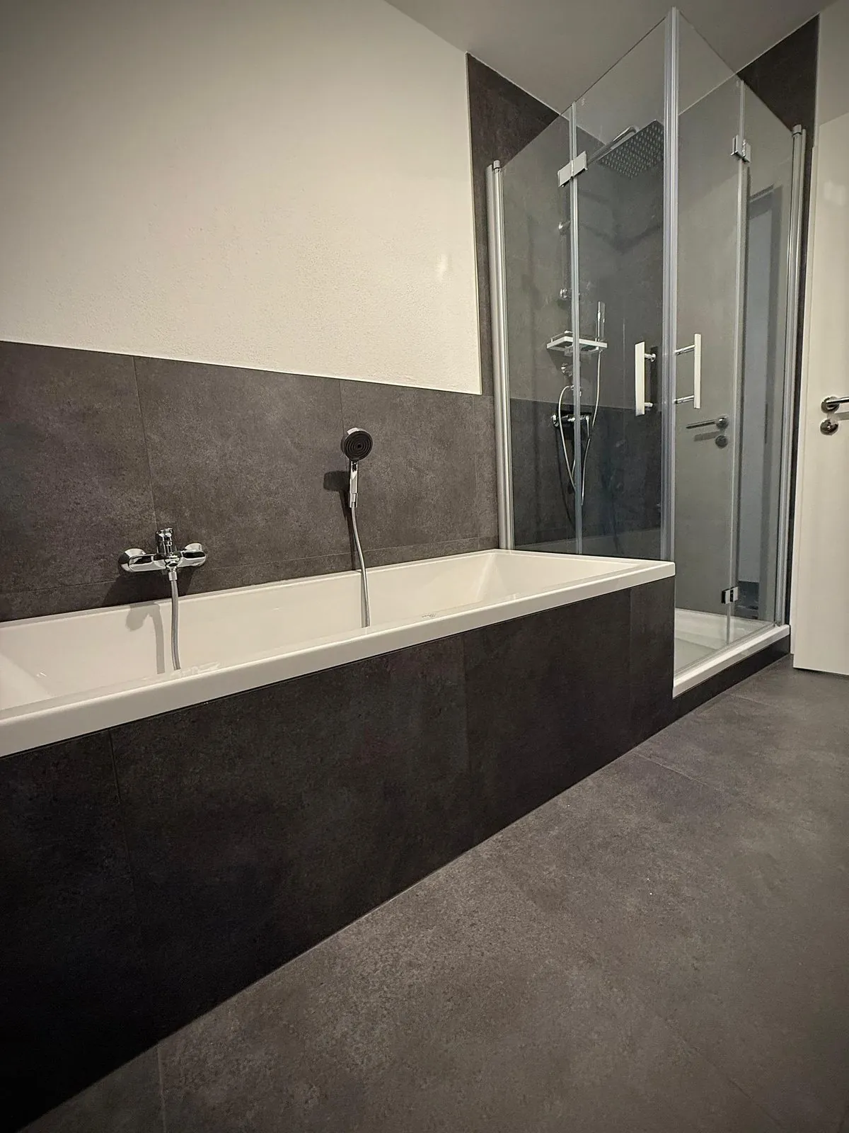 Badezimmer mit freistehender Badewanne vor dunklen Fliesen und separater Duschkabine mit Glastür, Projekt in Heidesheim am Rhein